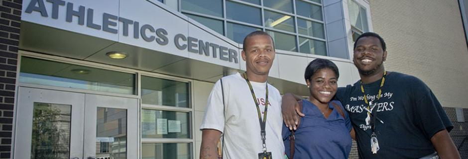 3 students, 2 of whom are wearing IDs around their necks, in front of Athletics Center