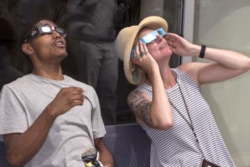 Two people in the crowd view the eclipse with eclipse glasses.