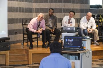 Panel members lean forward in their seats to see the presentation screen.