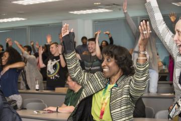 The audience raises their hands and jumps up with a smile at Mr. Sygielski's urging.