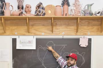 Roberto Lugo draws on a chalk board, demonstrating his technique