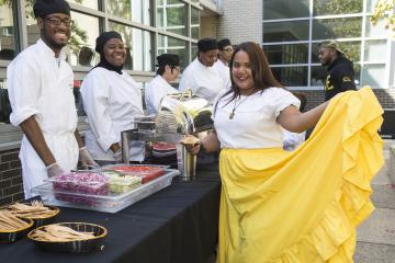 A performer, posing for the camera in a bright yellow skirt, is served food.