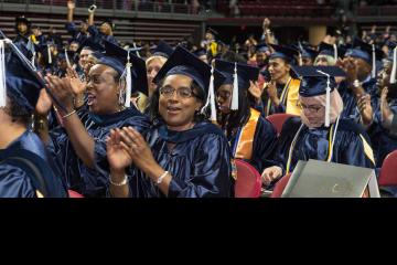 A crowd shot of graduates clapping and smiling.